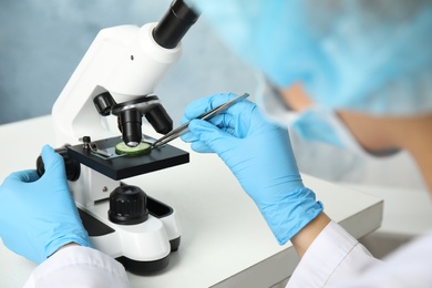 Photo of Scientist inspecting slice of cucumber with microscope in laboratory, closeup. Poison detection