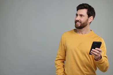 Photo of Smiling man with smartphone on grey background. Space for text