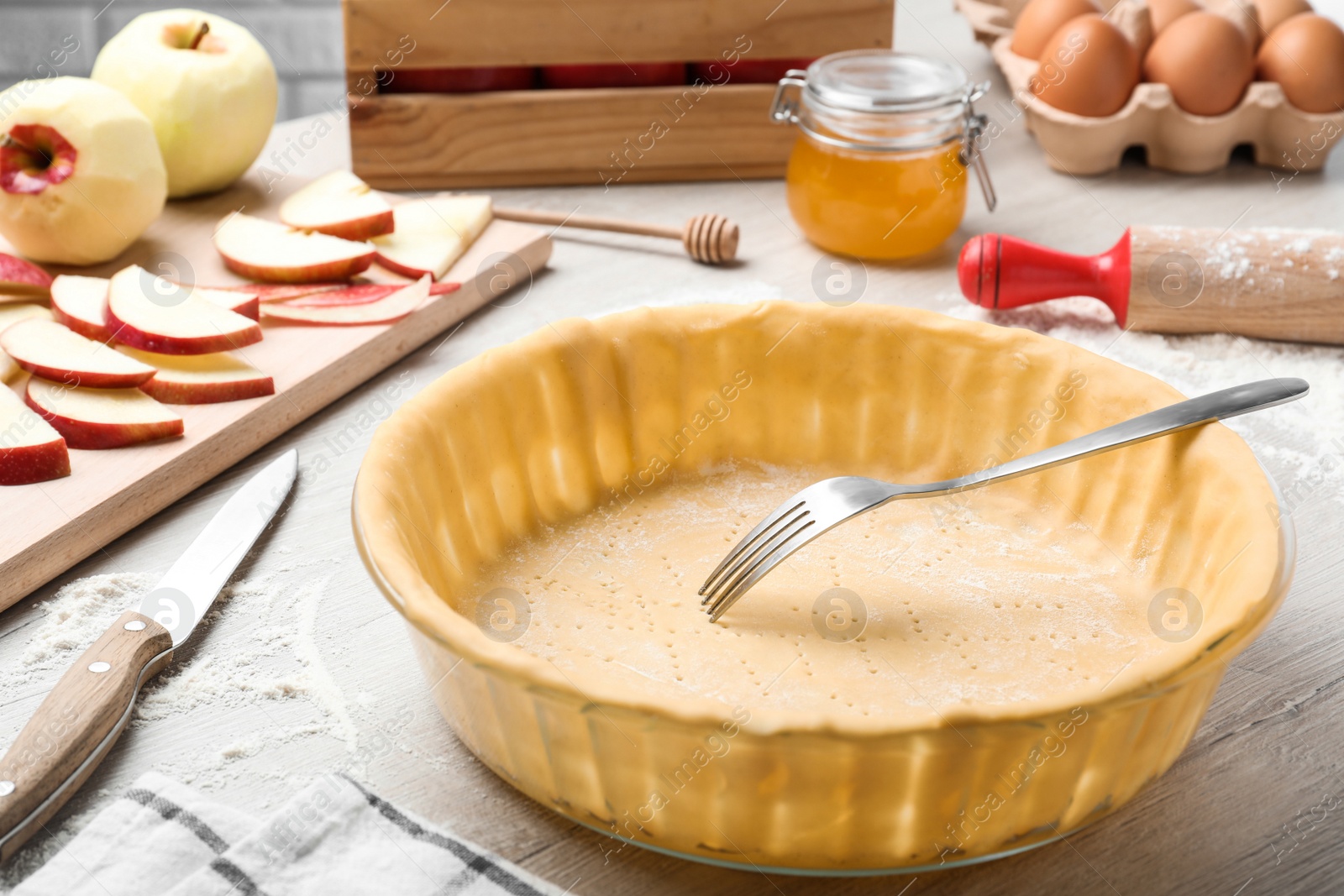 Photo of Raw dough with fork and ingredients on white wooden table. Baking apple pie