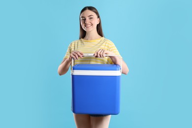 Happy young woman with plastic cool box on light blue background