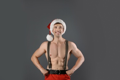 Young muscular man in Santa hat on gray background