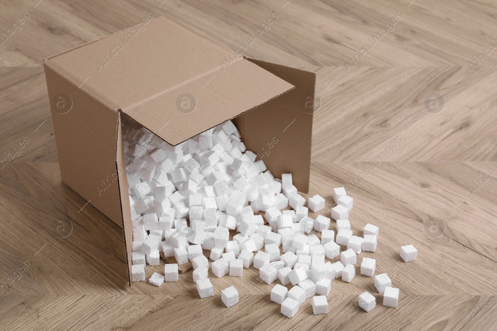 Photo of Overturned cardboard box with styrofoam cubes on wooden floor