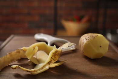 Photo of Wooden board with potato, peels and peeler on table, closeup