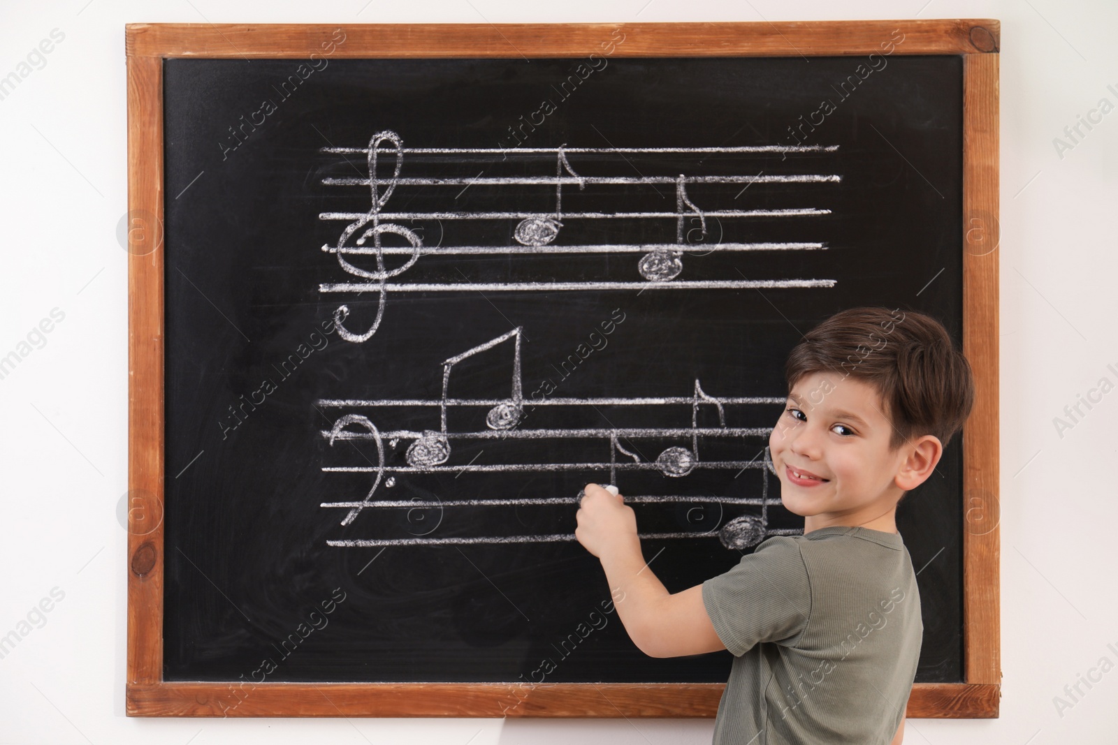 Photo of Little boy writing music notes on blackboard in classroom