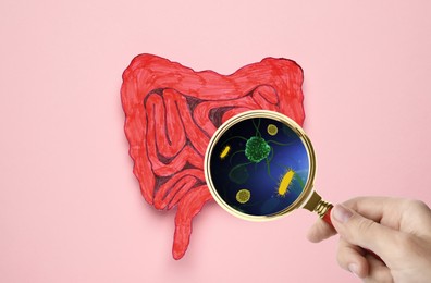 Microorganisms research. Woman with magnifying glass and paper intestine cutout on pink background, top view