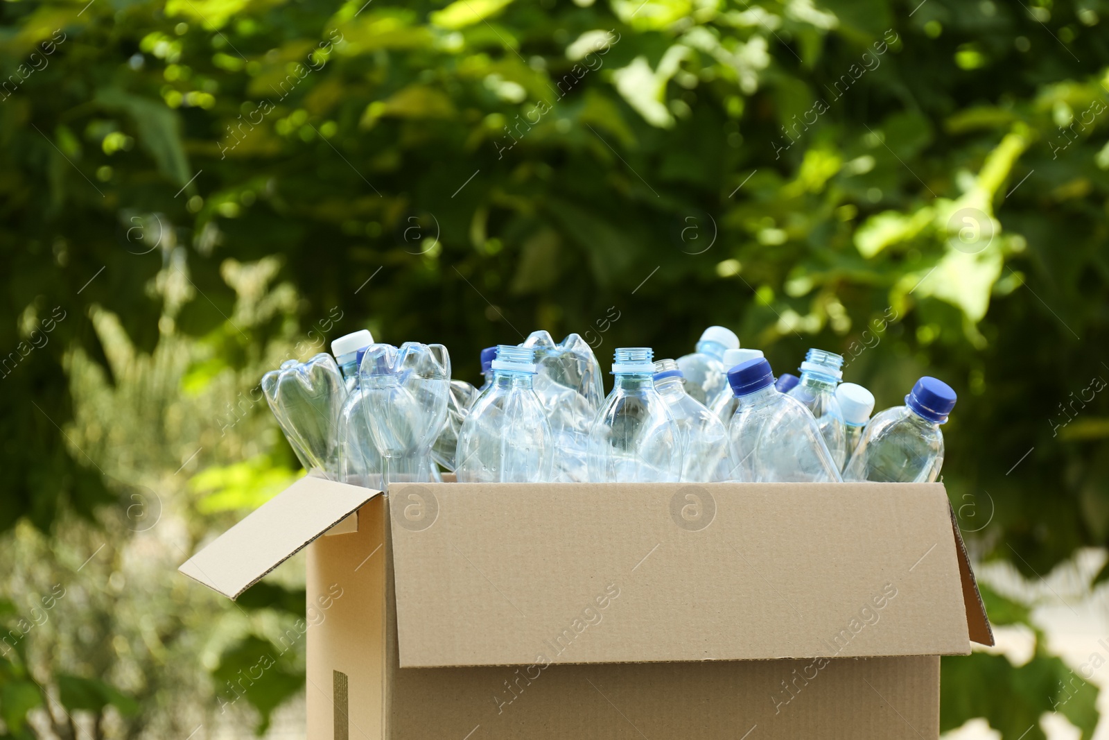 Photo of Cardboard box with used plastic bottles outdoors. Recycle concept