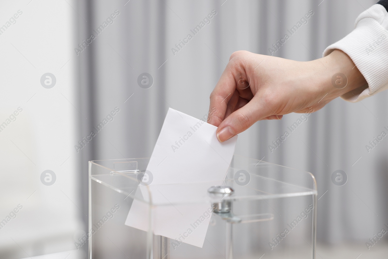 Photo of Woman putting her vote into ballot box on blurred background, closeup