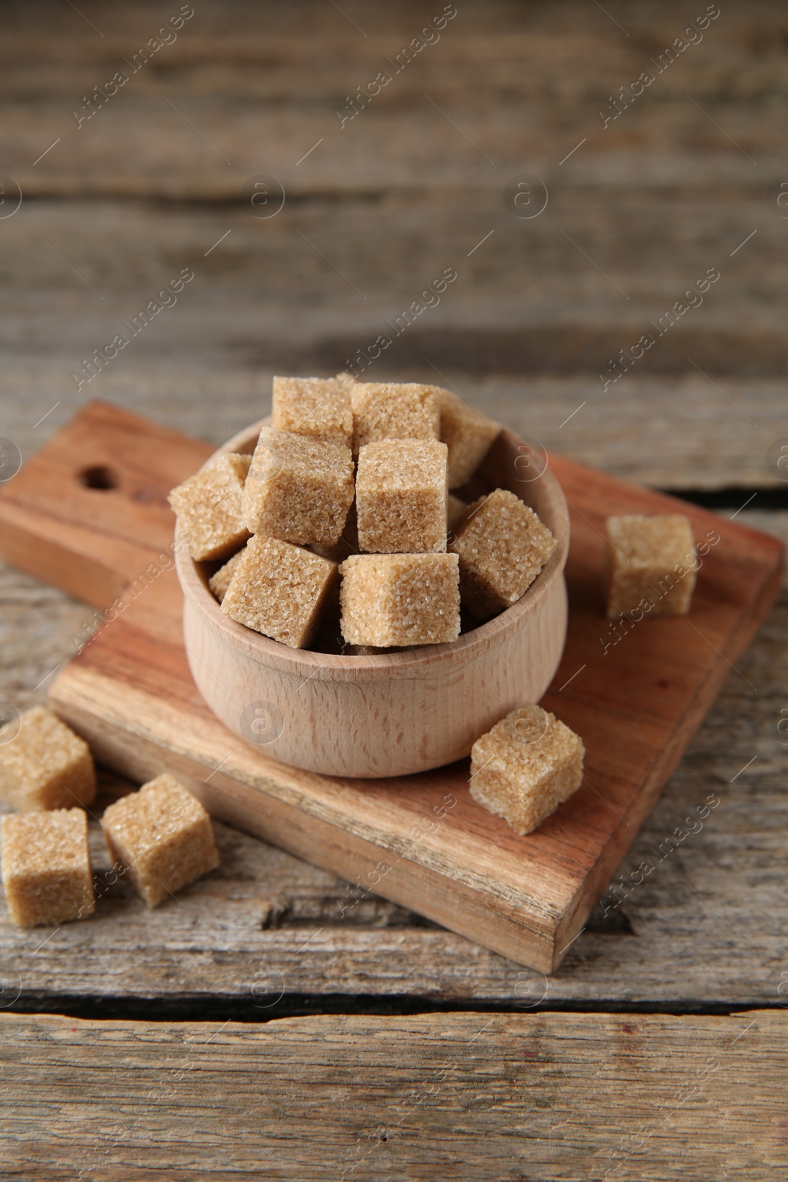 Photo of Brown sugar cubes in bowl on wooden table, closeup