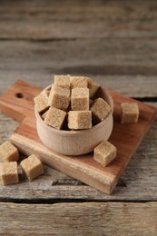 Photo of Brown sugar cubes in bowl on wooden table, closeup