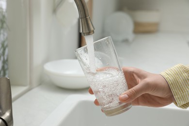 Photo of Woman filling glass with water from tap in kitchen, closeup