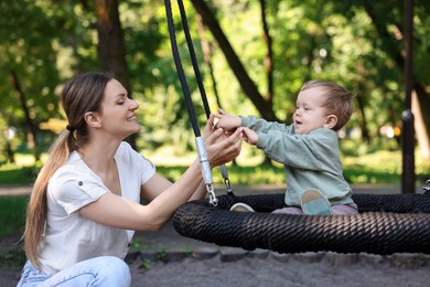 Photo of Happy nanny and cute little boy on swing outdoors