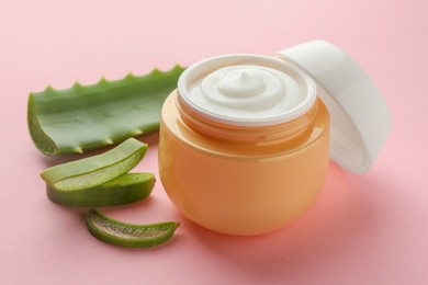 Jar with cream and cut aloe leaf on pink background, closeup