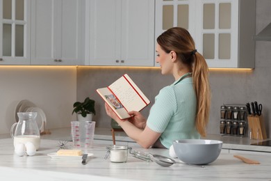 Woman with recipe book near table in kitchen