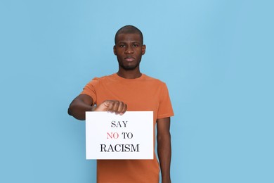 Photo of African American man holding sign with phrase Say No To Racism on light blue background