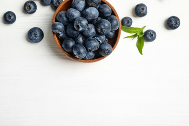 Fresh ripe blueberries in bowl on white wooden table, flat lay. Space for text