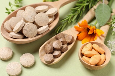 Photo of Different pills, herbs and flowers on light green background, closeup. Dietary supplements