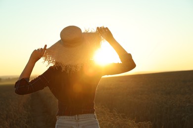Woman wearing straw hat in ripe wheat field on sunny day, back view