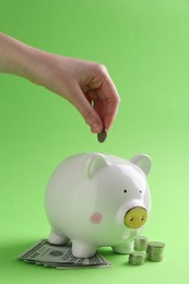 Photo of Financial savings. Woman putting coin into piggy bank on green background, closeup