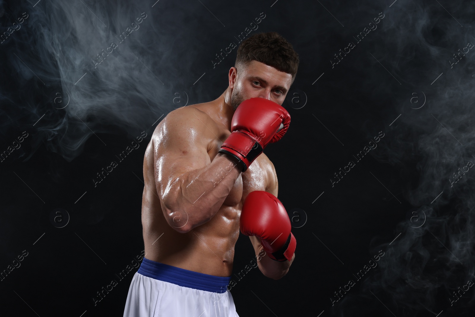 Photo of Man wearing boxing gloves in smoke on black background. Space for text