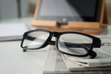 Photo of Stack of newspapers and glasses on white table indoors, closeup