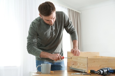 Photo of Young working man repairing drawer at home