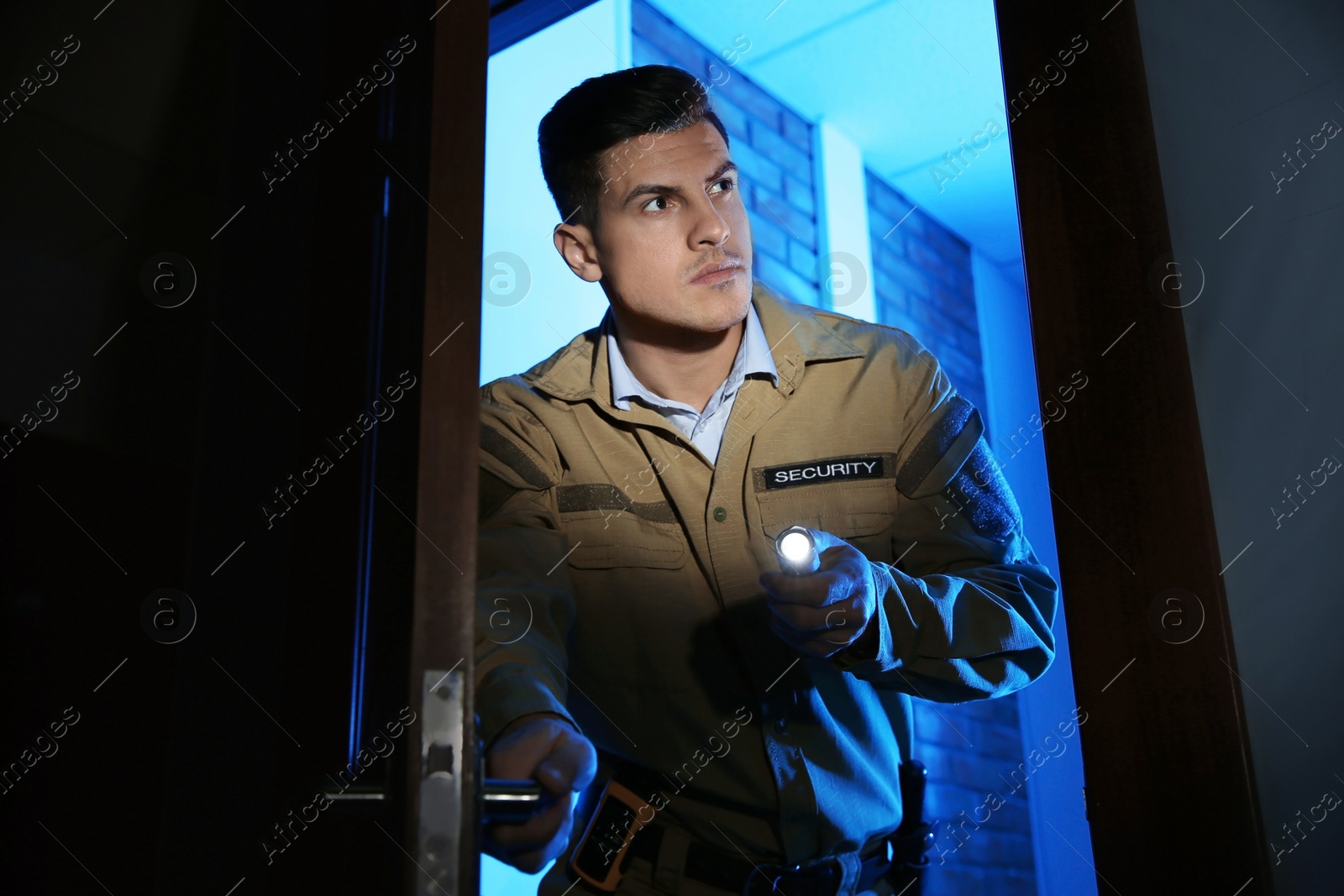 Photo of Professional security guard with flashlight checking dark room