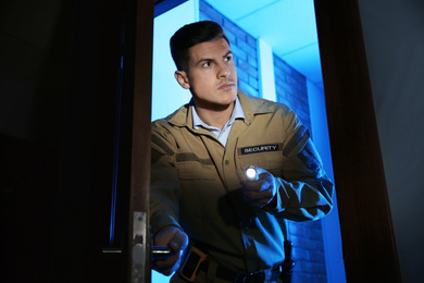 Photo of Professional security guard with flashlight checking dark room