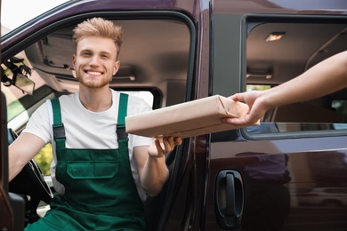 Photo of Young delivery courier giving parcel to customer outdoors