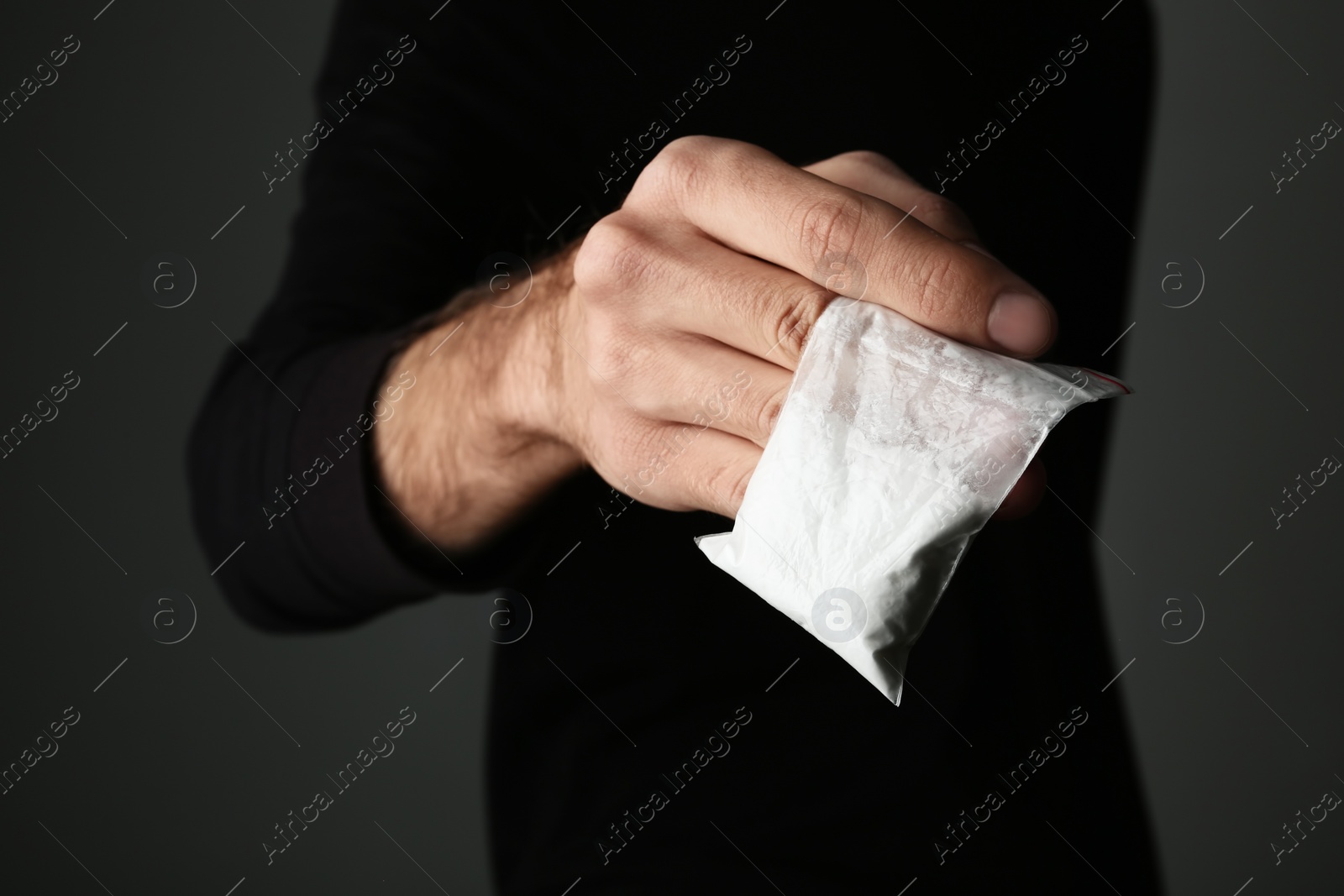 Photo of Drug dealer holding bag with cocaine on dark background, closeup