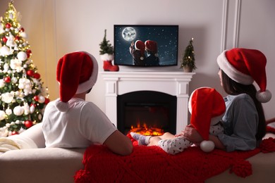 Image of Family watching TV movie in room decorated for Christmas, back view