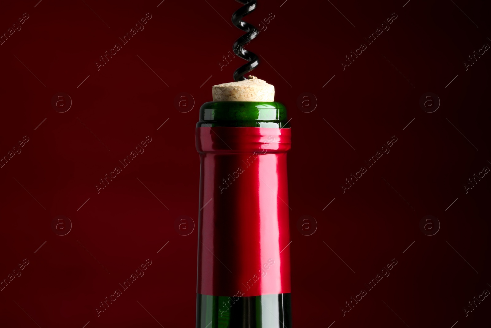 Photo of Opening bottle of wine with corkscrew on burgundy background