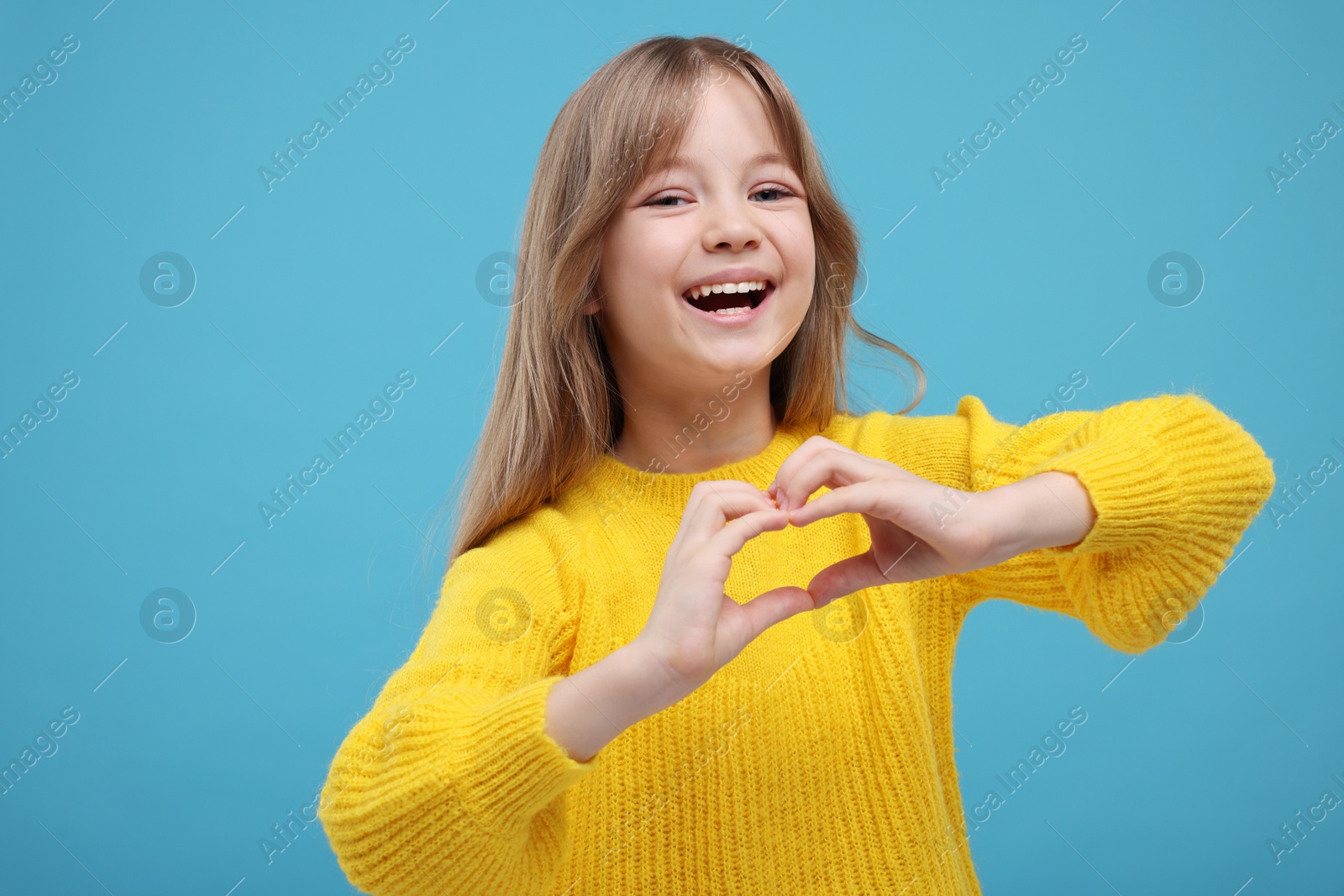 Photo of Happy girl showing heart gesture with hands on light blue background