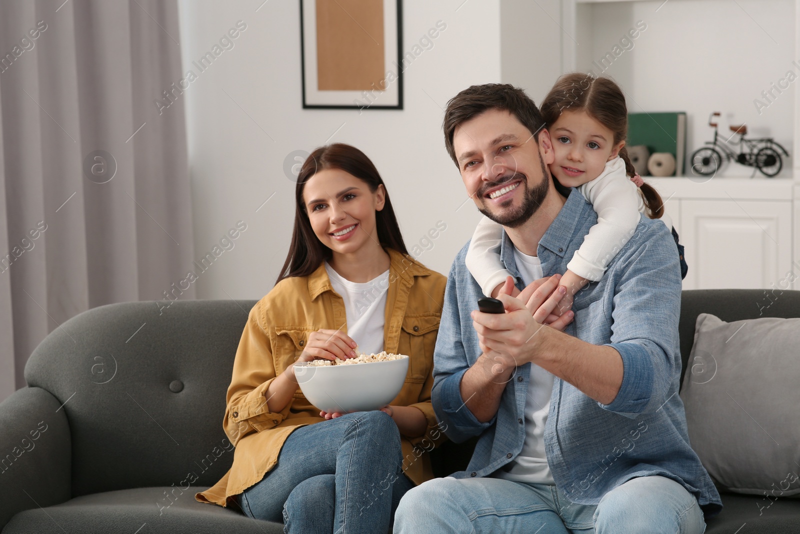 Photo of Happy family watching movie at home. Father changing TV channels with remote control