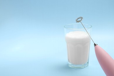 Photo of Mini mixer (milk frother) and whipped milk in glass on light blue background. Space for text