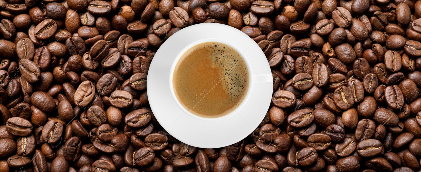 Image of Cup of tasty aromatic coffee on roasted beans, top view. Banner design