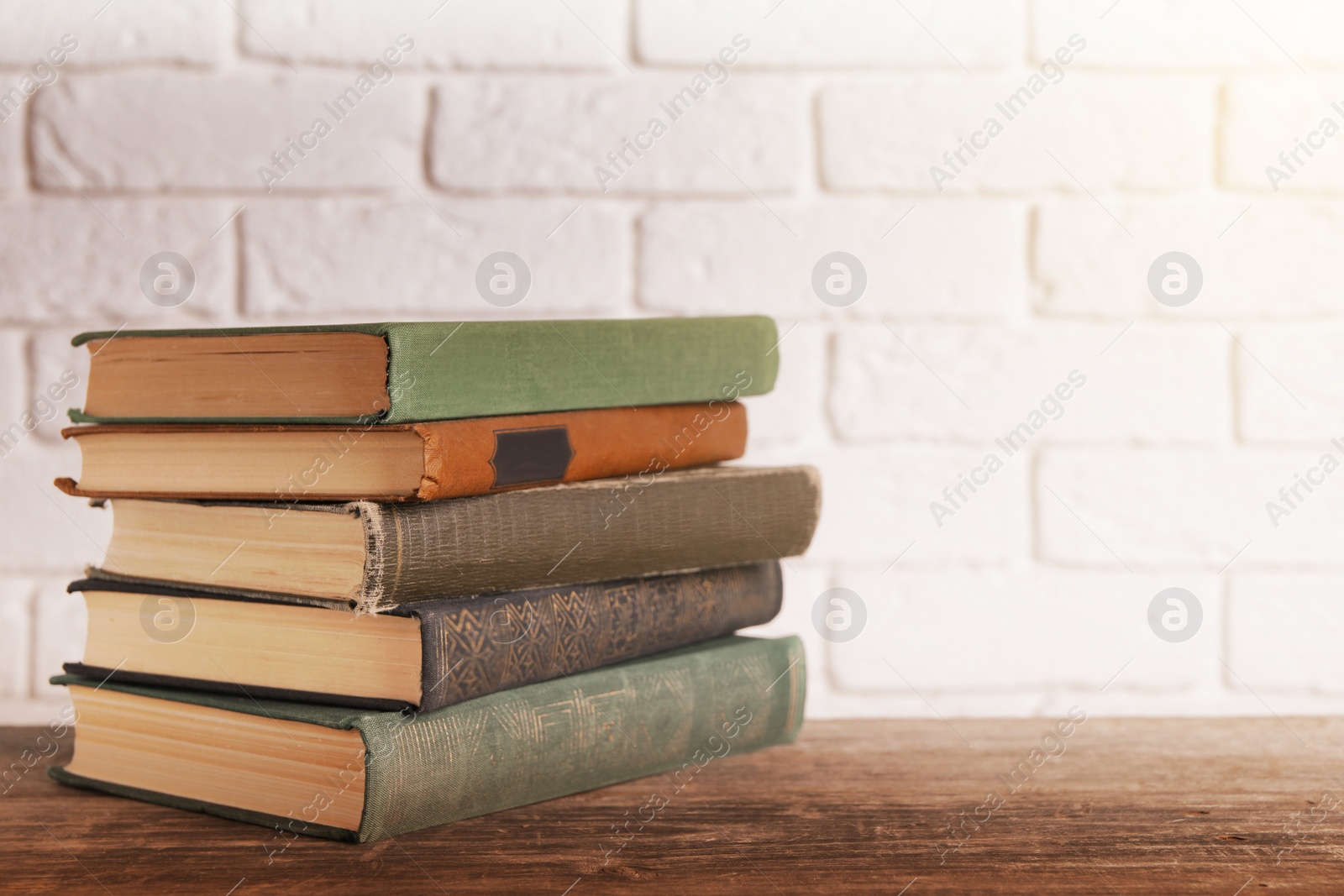 Image of Stack of old hardcover books on wooden table near white brick wall, space for text