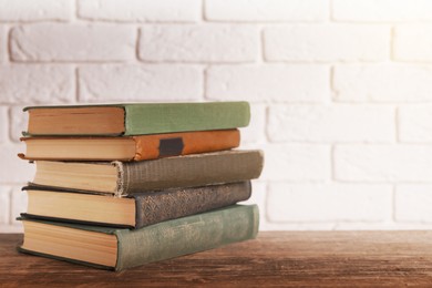 Image of Stack of old hardcover books on wooden table near white brick wall, space for text