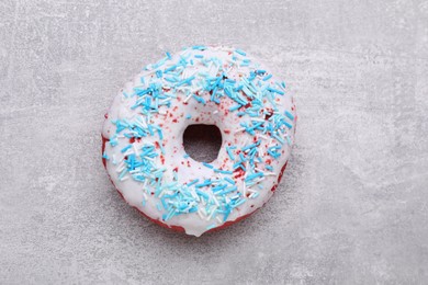 Sweet glazed donut decorated with sprinkles on light grey table, top view. Tasty confectionery