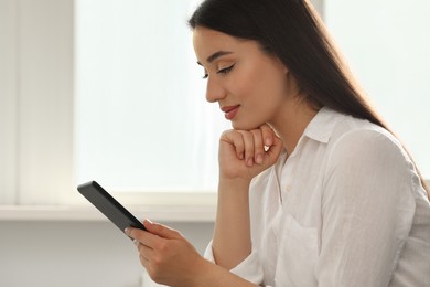 Photo of Young woman using e-book reader at home
