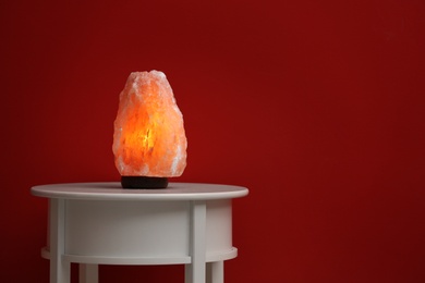 Photo of Himalayan salt lamp on table against dark red background. Space for text