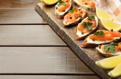 Photo of Tasty canapes with salmon, capers, lemon and cream cheese on wooden table, closeup. Space for text