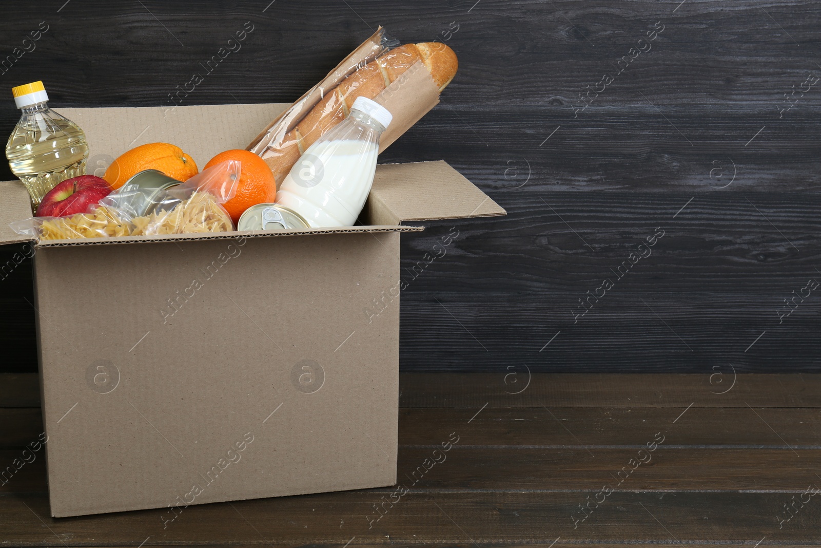 Photo of Cardboard box with donation food on wooden table, closeup. Space for text