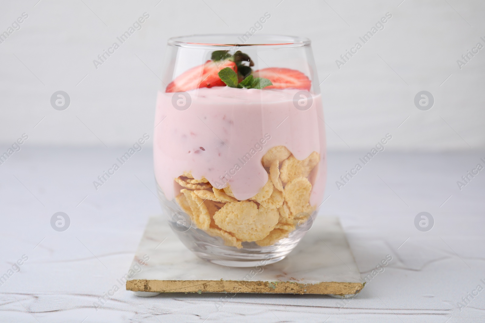 Photo of Glass with yogurt, strawberries and corn flakes on white textured table