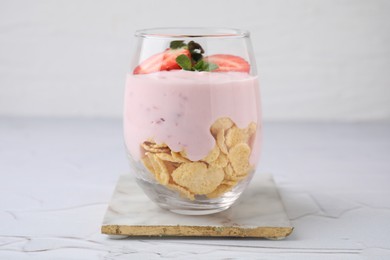 Glass with yogurt, strawberries and corn flakes on white textured table