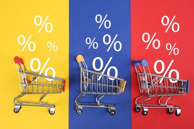 Image of Discount offer. Mini shopping carts and percent signs on colorful background, top view