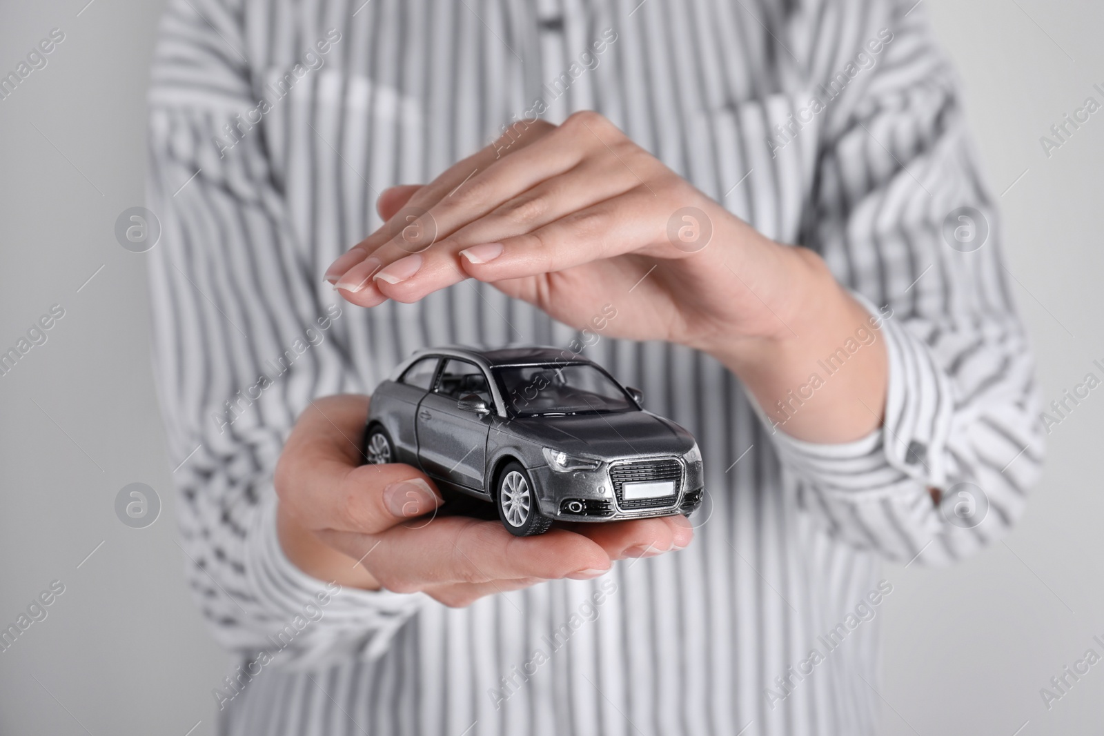 Photo of Insurance agent covering toy car on grey background, closeup