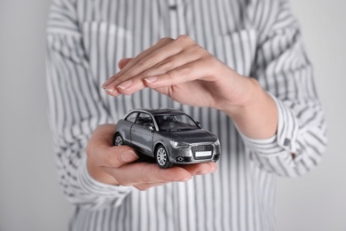 Photo of Insurance agent covering toy car on grey background, closeup