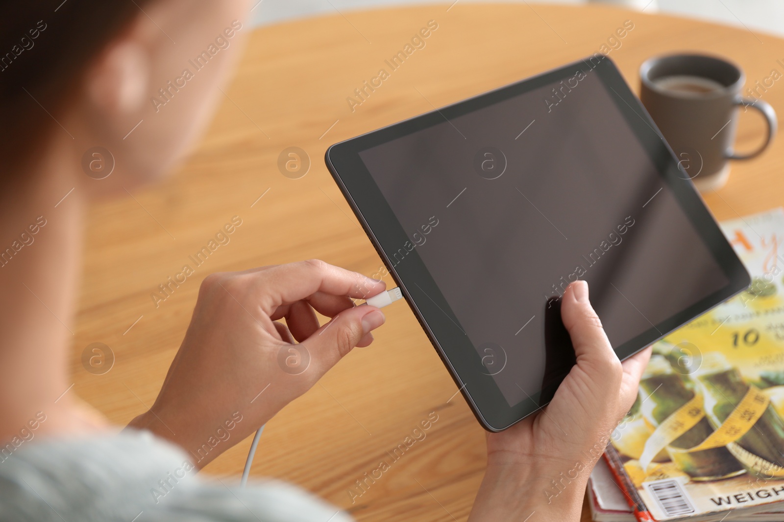 Photo of Woman connecting charger cable to tablet at wooden table, closeup