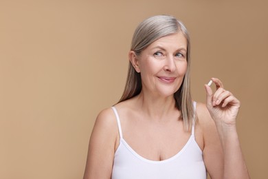 Photo of Beautiful woman with vitamin capsule on beige background, space for text