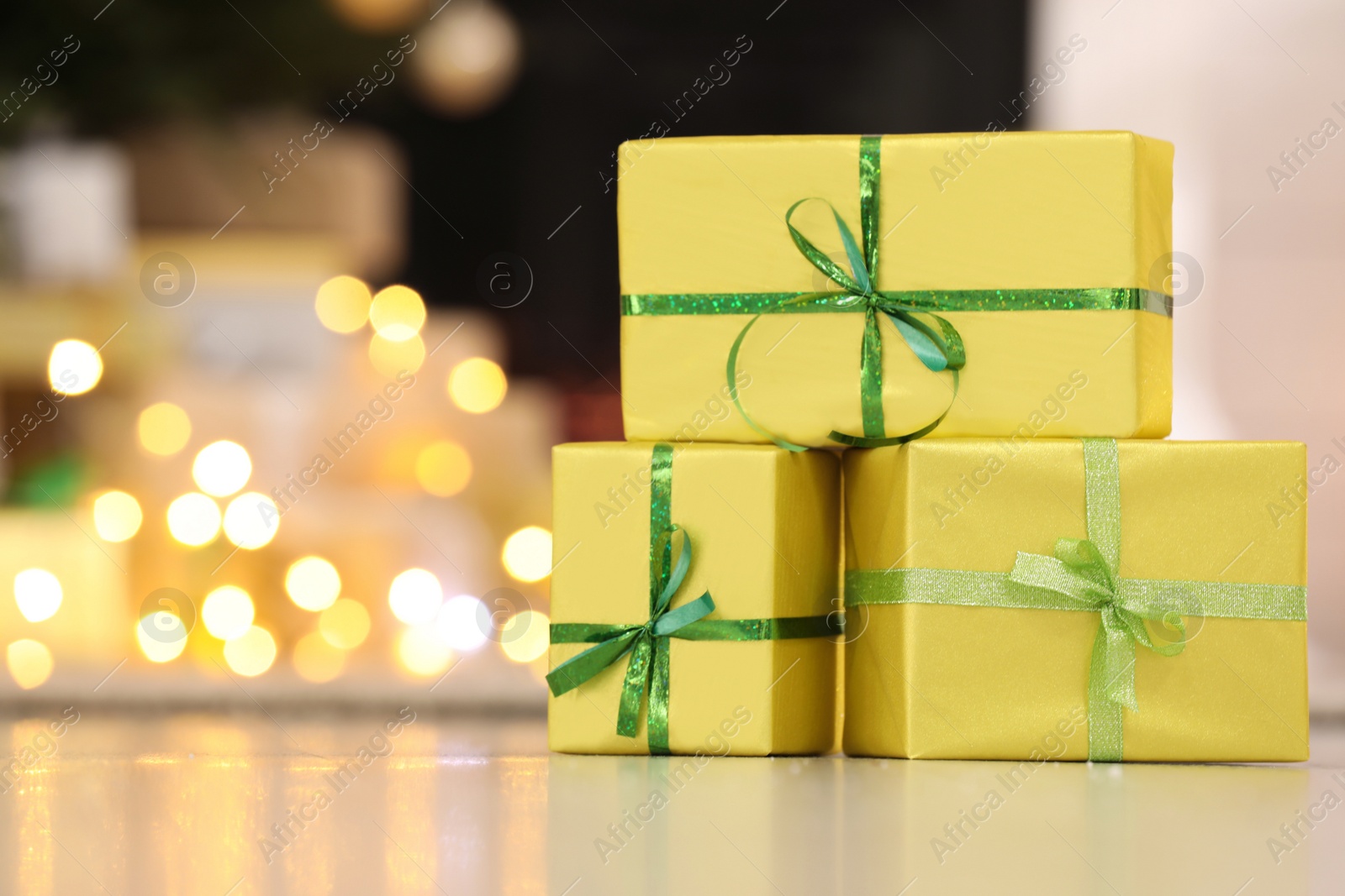 Photo of Beautifully wrapped gift boxes against blurred festive lights, space for text. Christmas celebration
